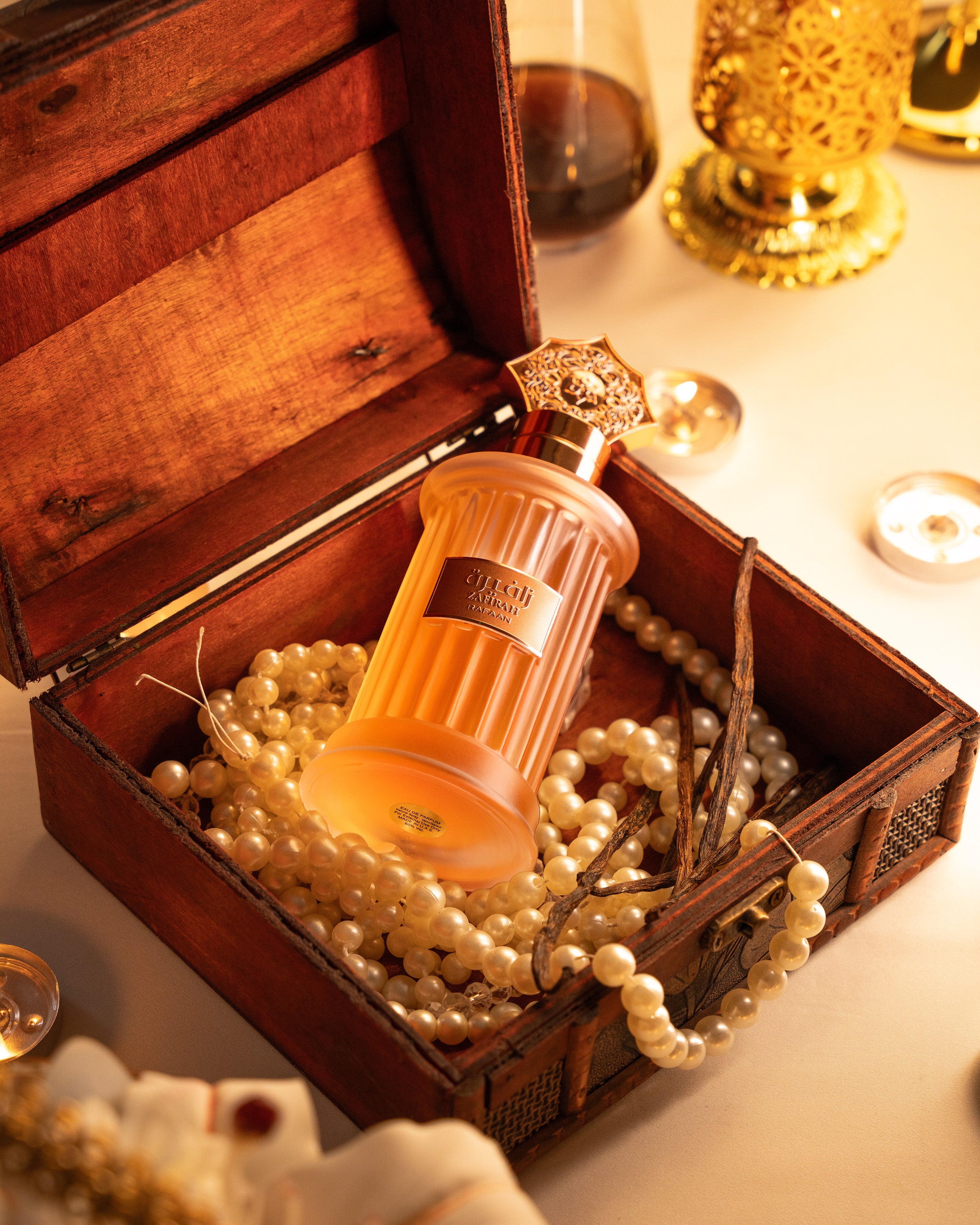 Perfume bottle in a wooden box with pearls and candles in the background